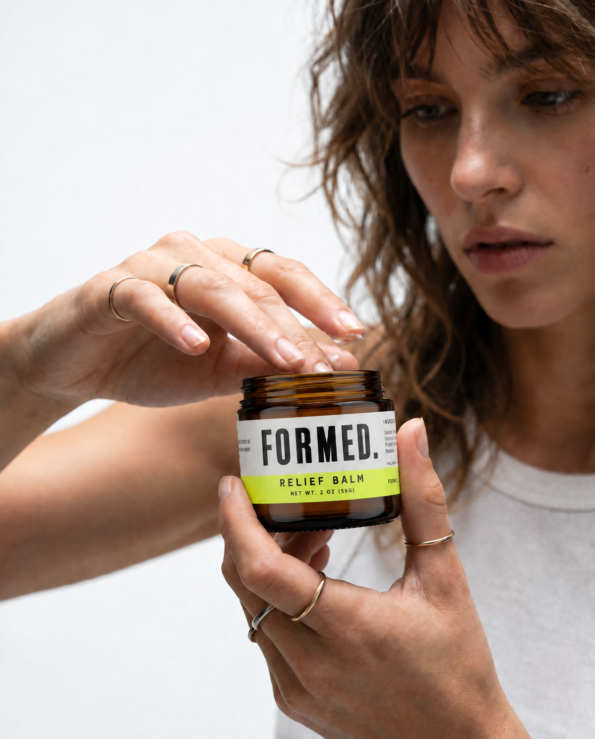 A woman holds an amber glass jar of Formed Relief Balm against a clean white background.